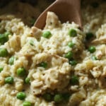 A wooden spoon is used to serve creamy chicken and rice with green peas.