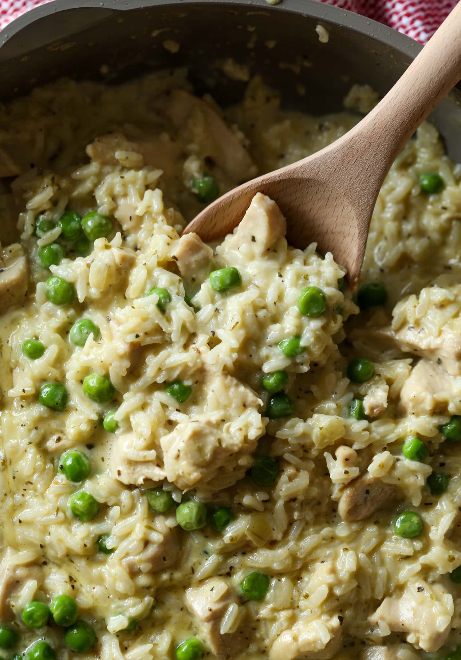 A wooden spoon is used to serve creamy chicken and rice with green peas.