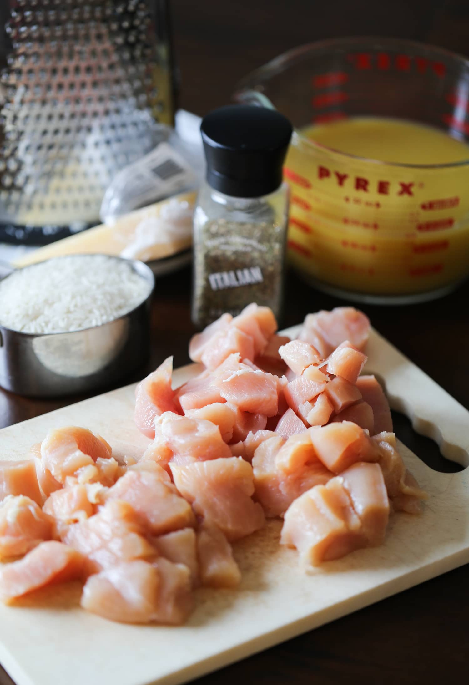 Diced chicken on a cutting board, next to seasoned salt and pepper.