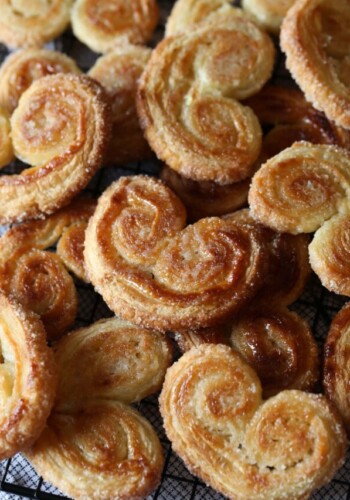 An assortment of crunchy and golden palmiers piled over a wire rack.