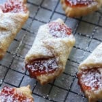 A close up of kolaczki cookies filled with strawberry preserves and dusted with powdered sugar.