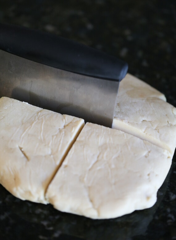 Kolaczki cookie dough is divided into quarters using a steel dough scraper.