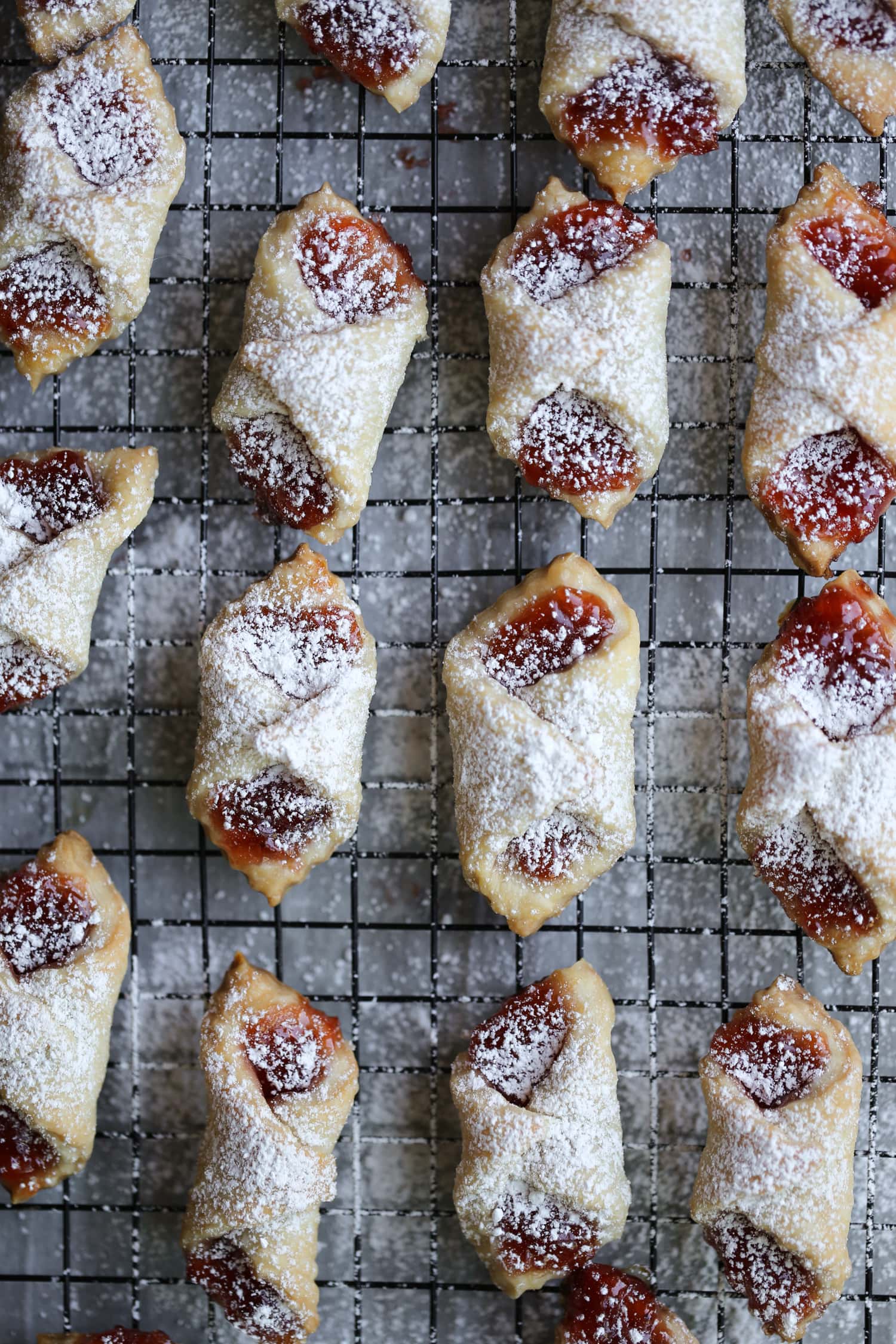 Filled and baked polish kolaczki cookies arranged in rows on a baking sheet, dusted with powdered sugar.