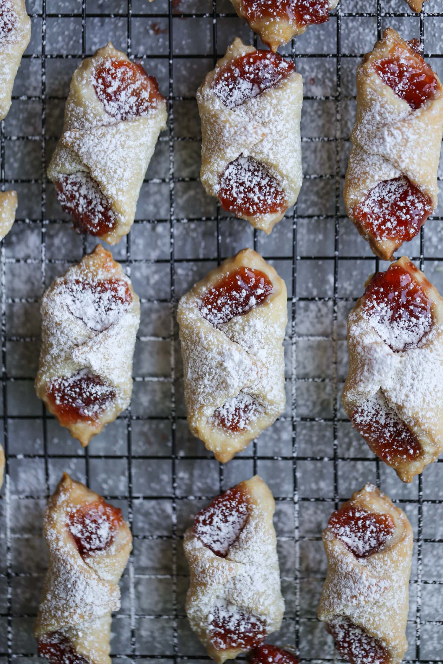Filled and baked polish kolaczki cookies arranged in rows on a baking sheet, dusted with powdered sugar.