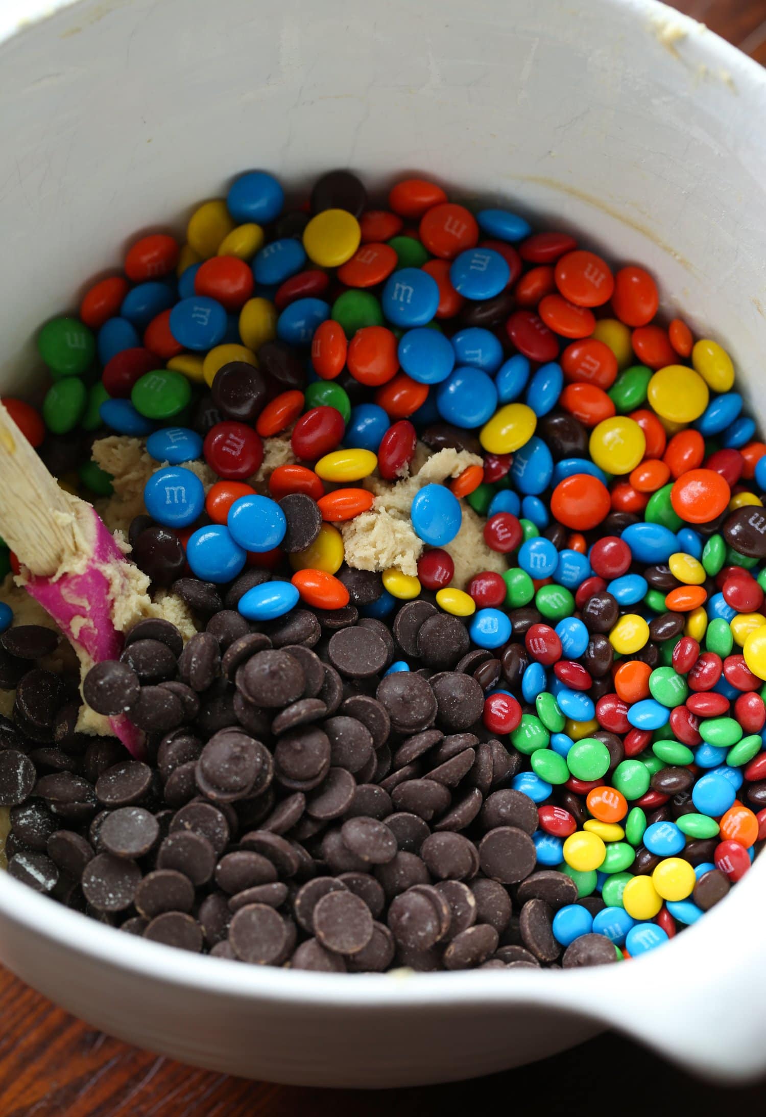 Mixing in M&Ms and chocolate chips in a bowl of cookie dough