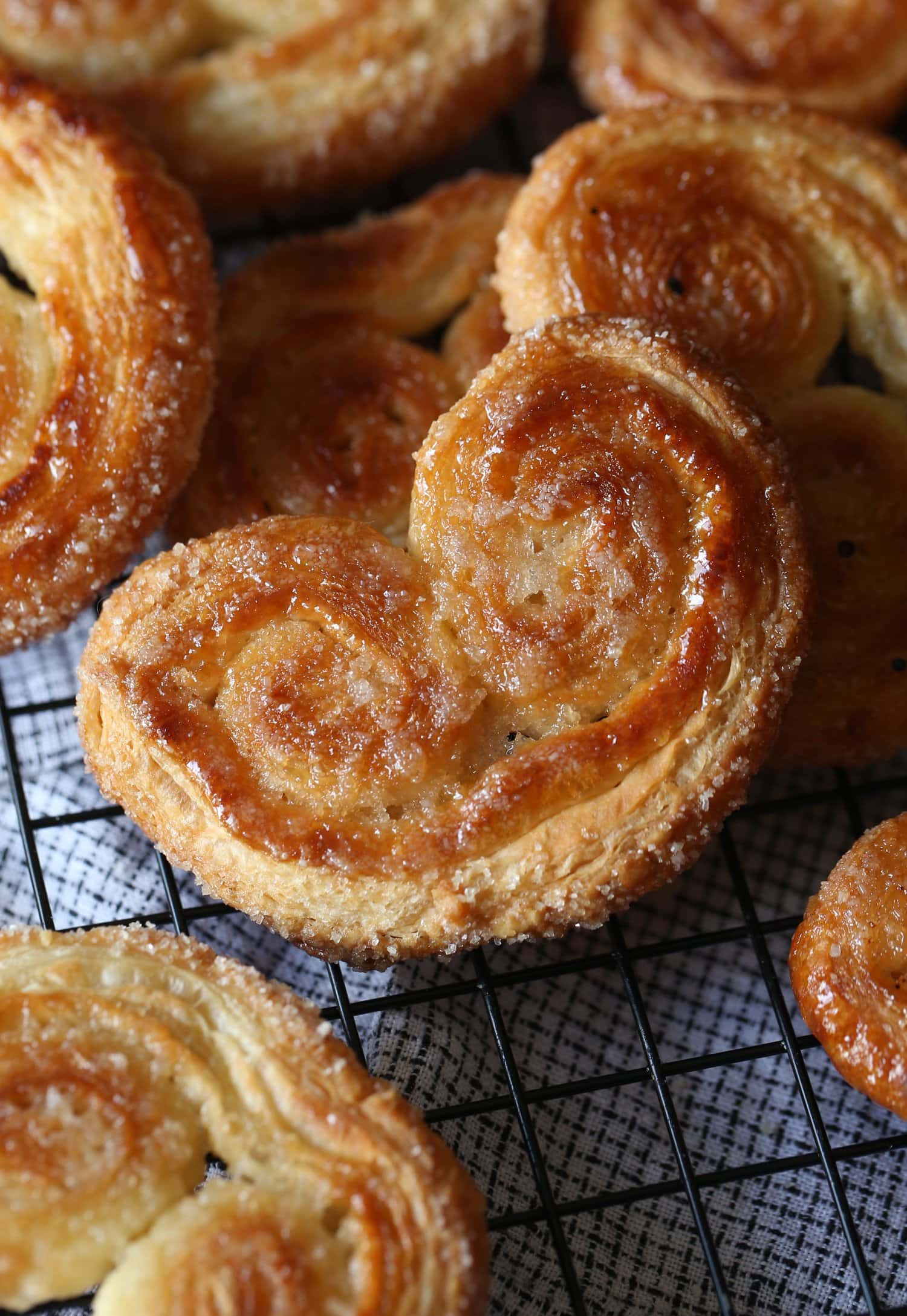 Crunchy and golden palmier cookies scattered on top of a wire rack.