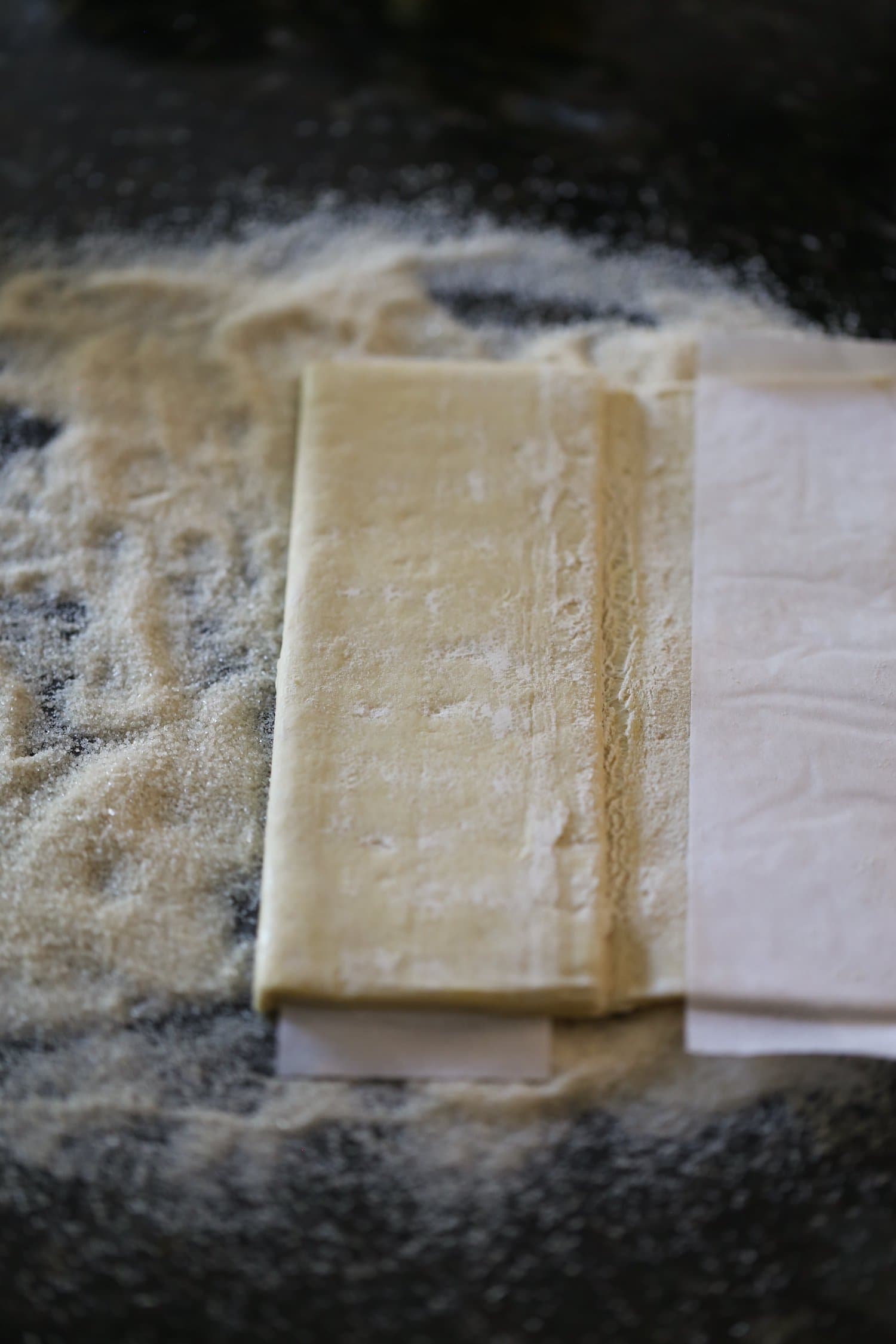 Folding Palmiers Dough Step 2: Thawed puff pastry is partially unfolded onto a sugar coated countertop.
