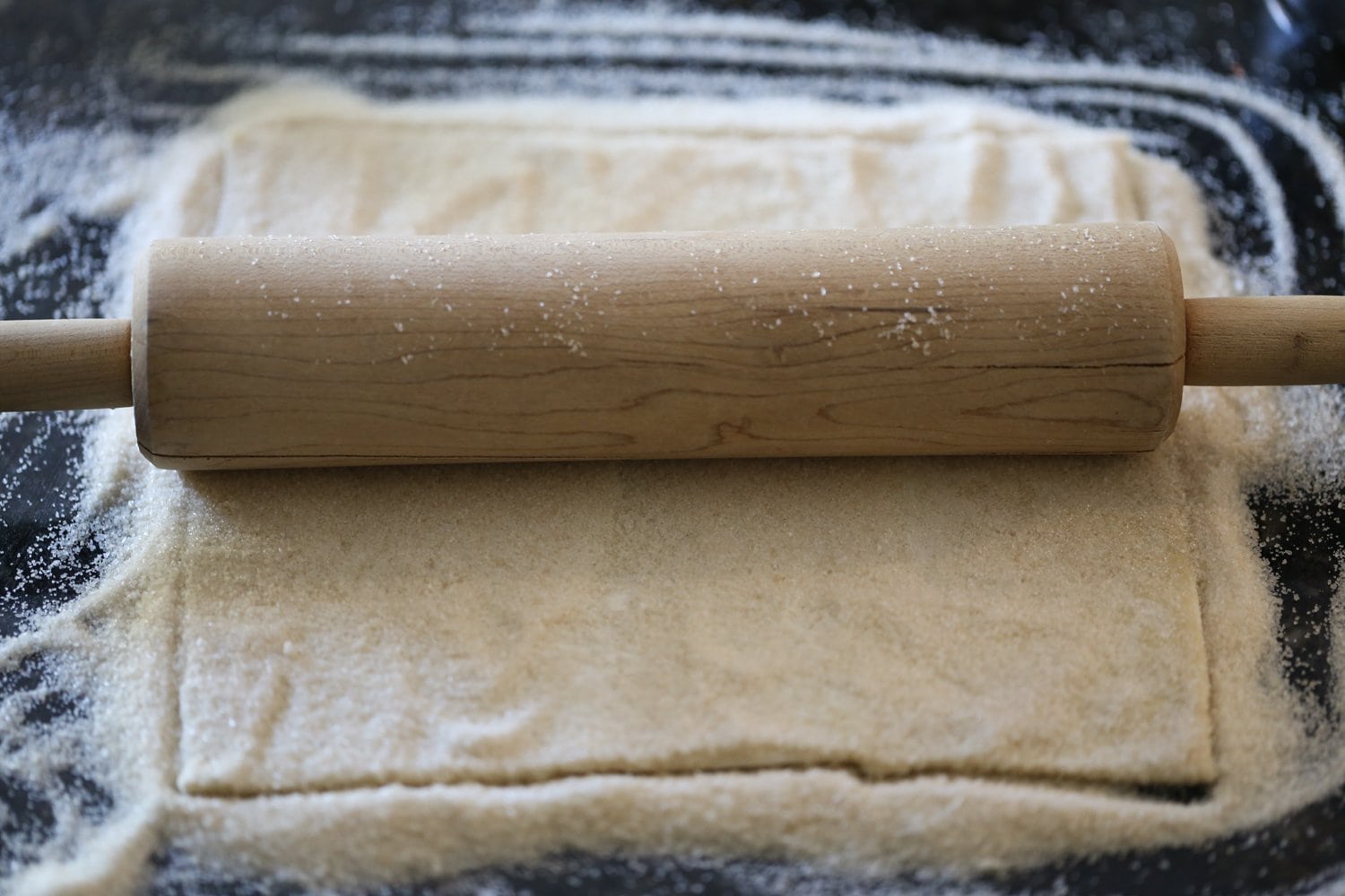 Folding Palmiers Dough Step 4: A rolling pin is used to roll out the pastry dough coated in sugar.