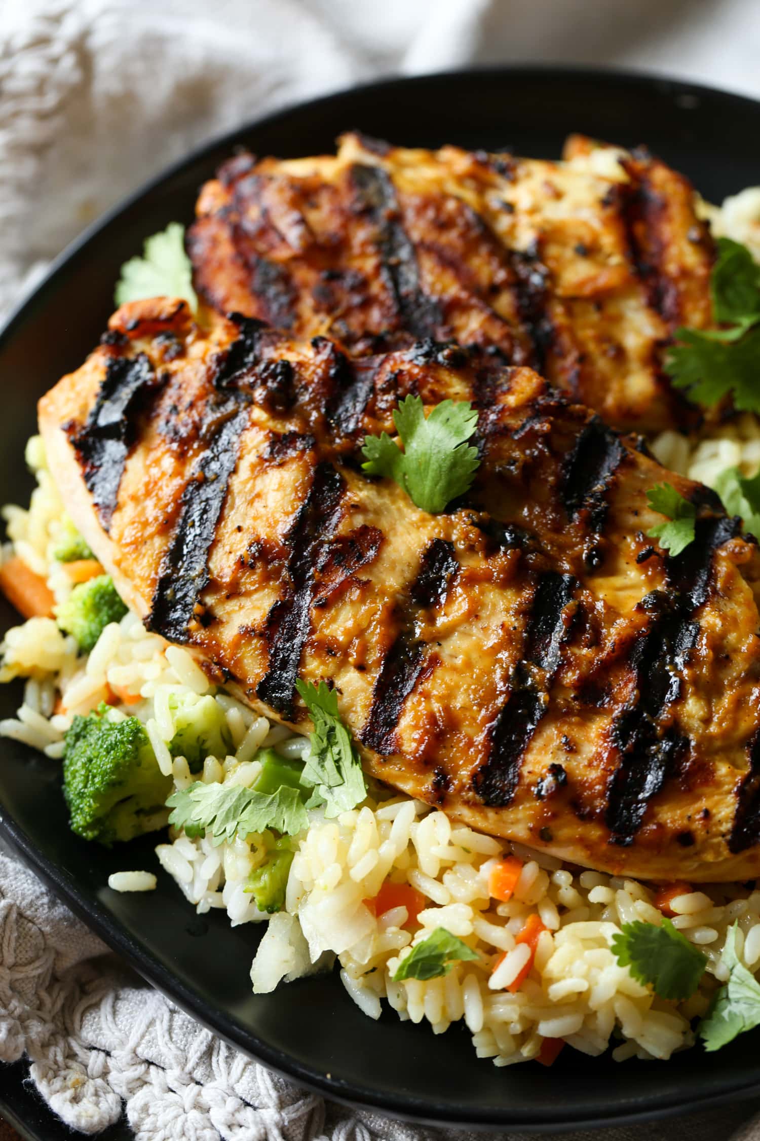 Grilled peanut butter chicken is served over a bed of rice and veggies.