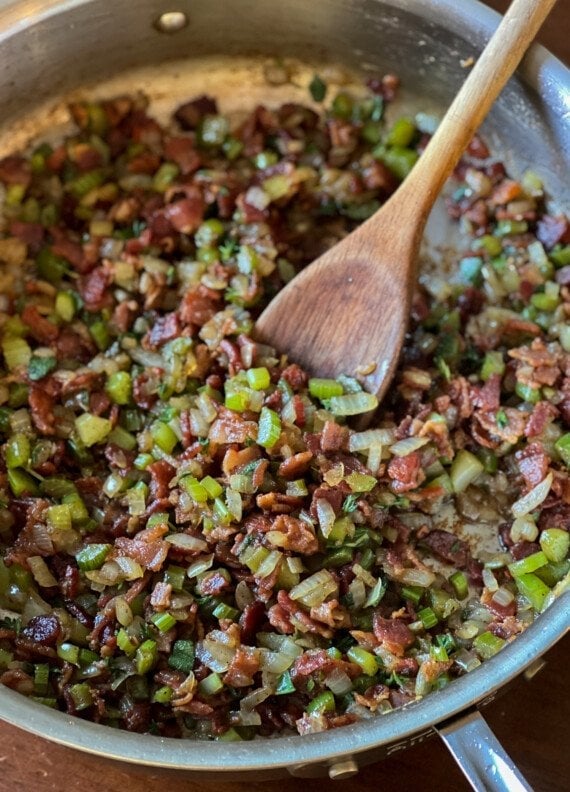 onions, celery, and bacon in a skillet with a wooden spoon