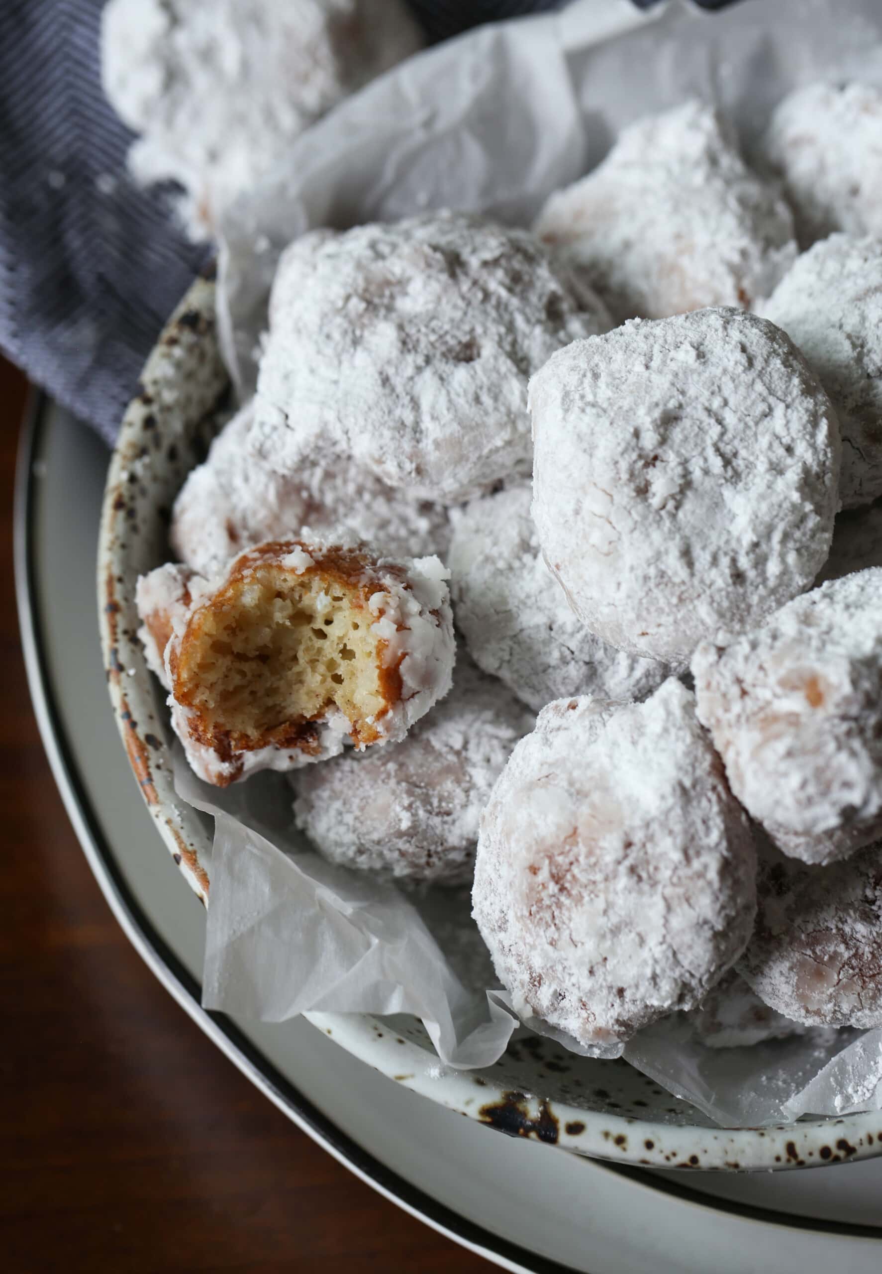 Sweet Calas in a bowl coated in powdered sugar with one cut in half showing interior