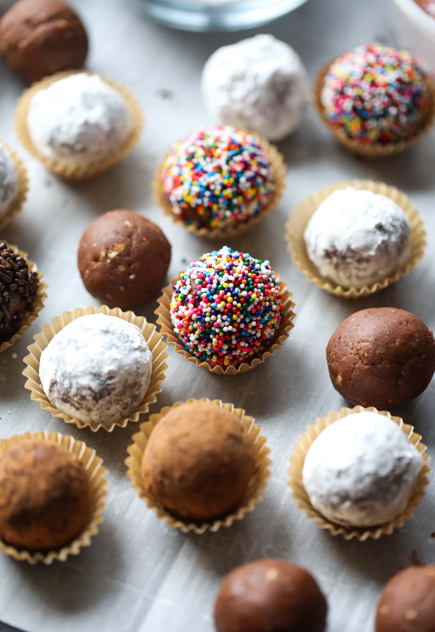 Holiday rum balls decorated with sprinkles, cocoa, and powdered sugar, placed in candy cups.