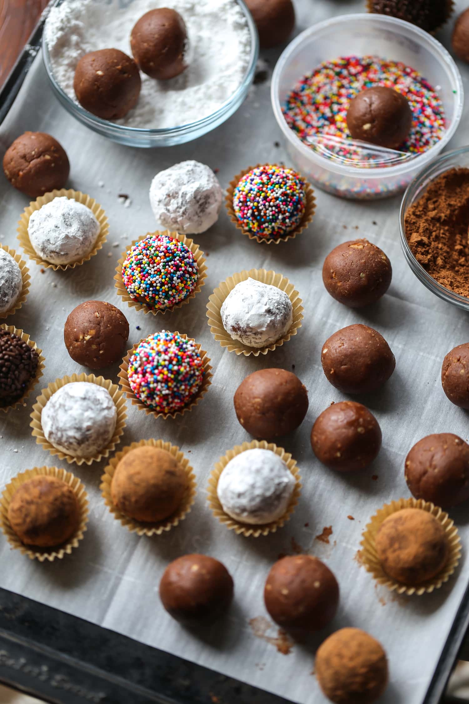 Holiday rum balls decorated with sprinkles, cocoa, and powdered sugar, placed in candy cups.