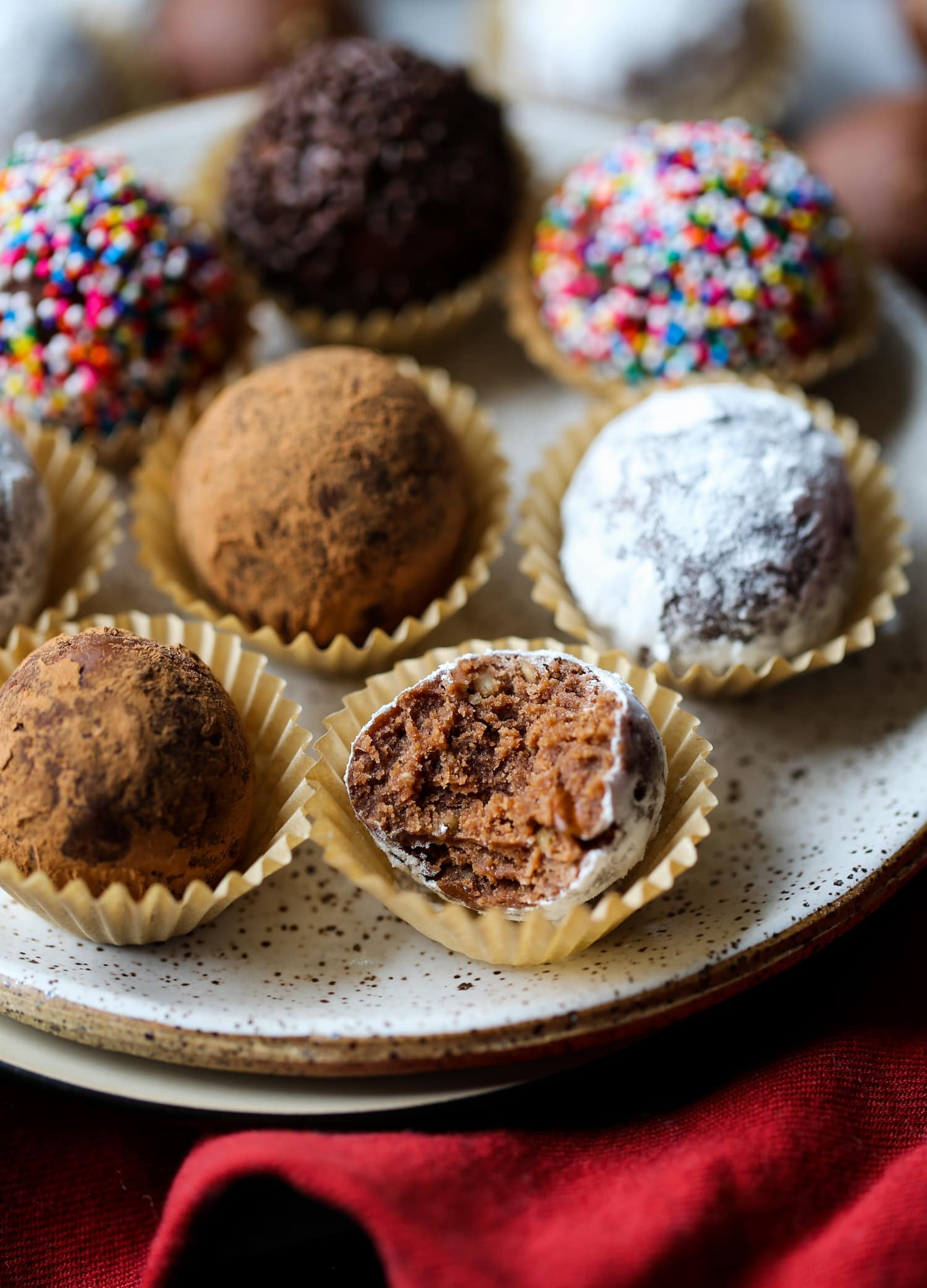 Decorated holiday rum balls in candy cups, arranged on a plate, one with a bite missing.