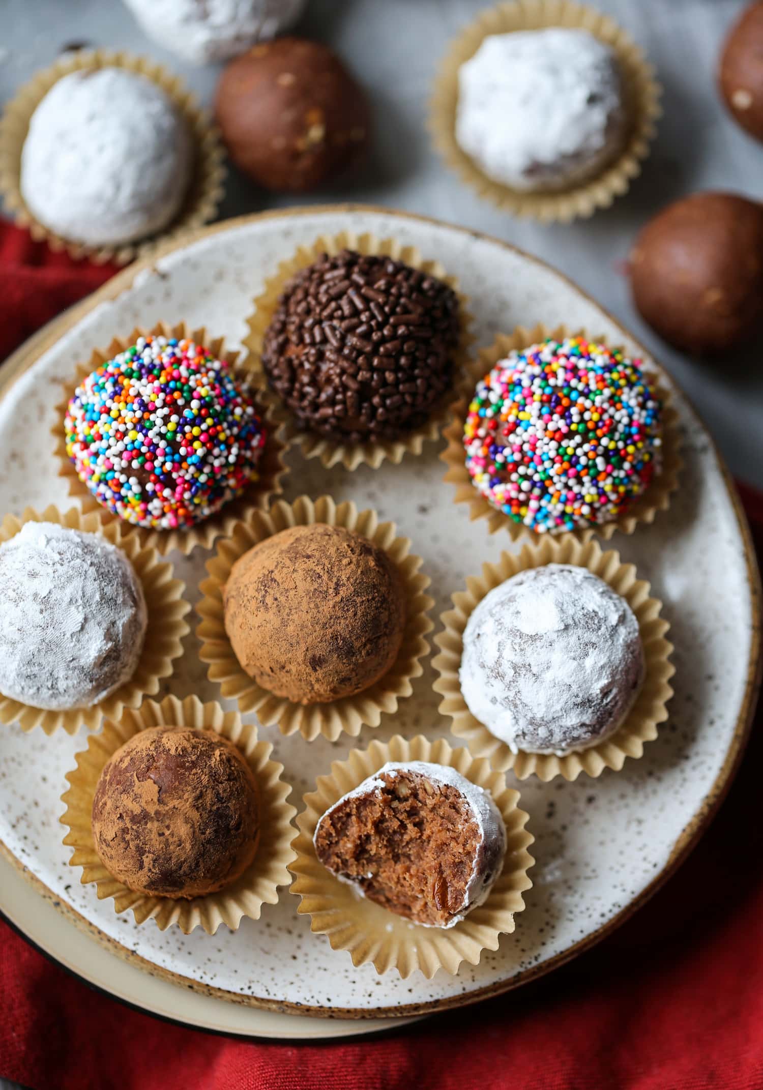 Decorated holiday rum balls in candy cups, arranged on a plate, one with a bite missing.