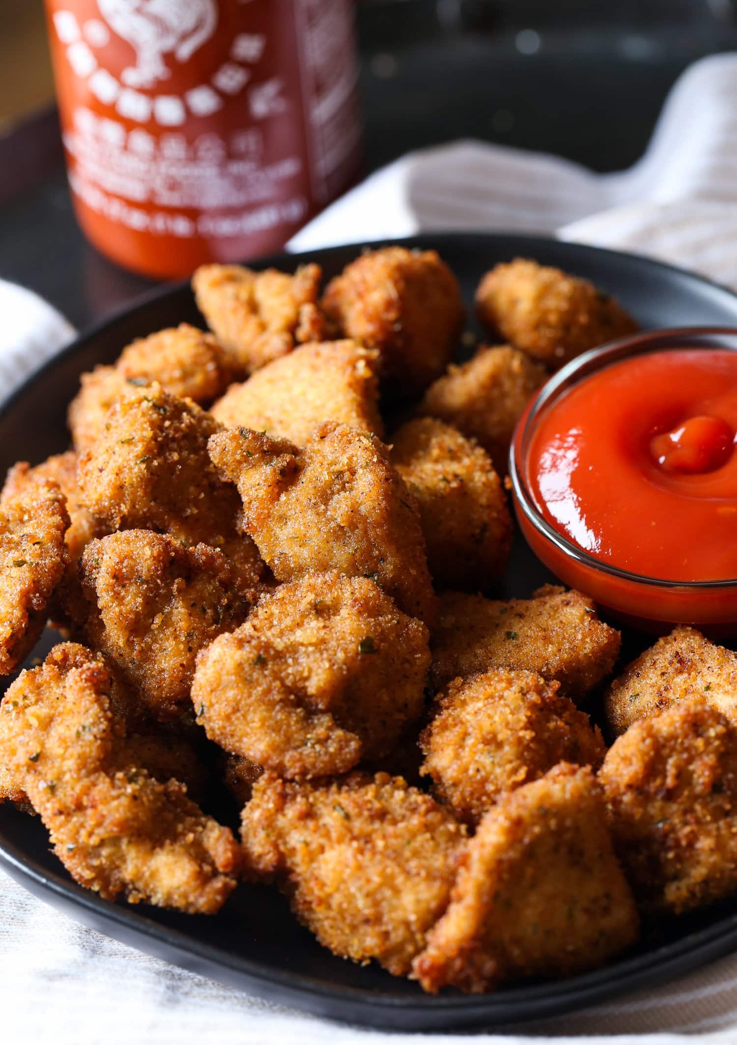 Spicy homemade chicken nuggets on a plate next to dipping sauce.