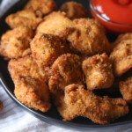 Spicy chicken nuggets on a plate next to a bowl of hot sauce for dipping.