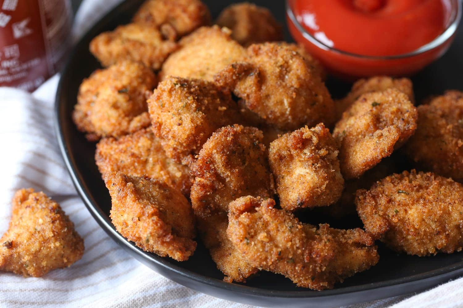 Spicy chicken nuggets on a plate next to a bowl of hot sauce for dipping.