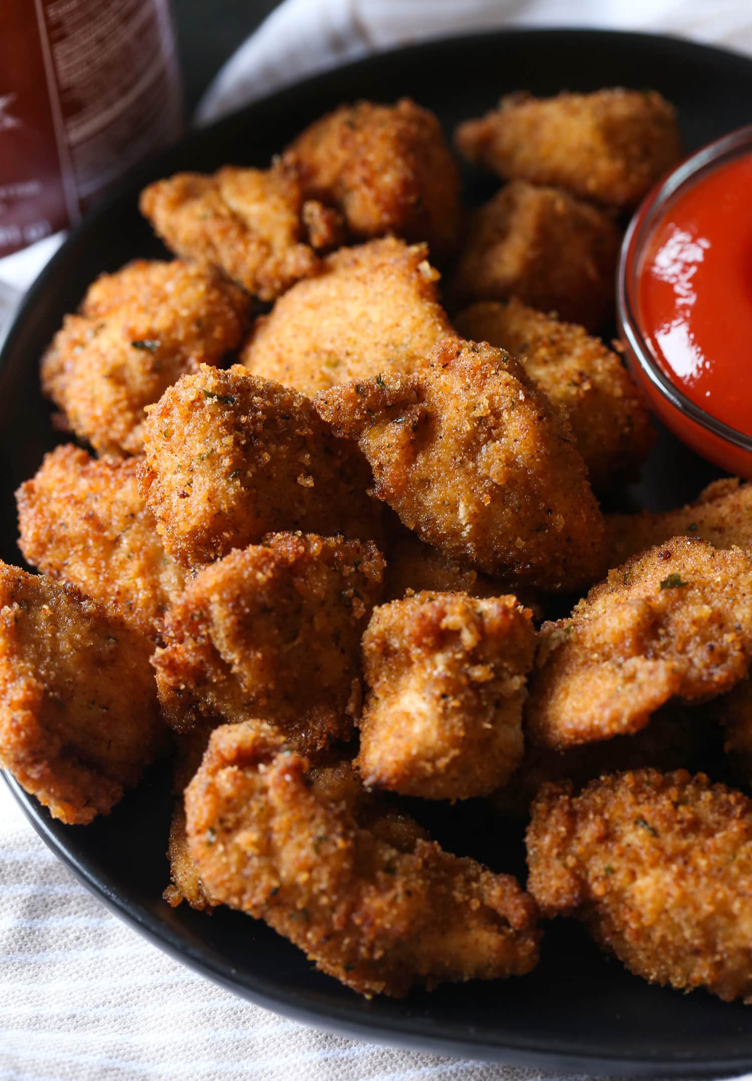 Spicy homemade chicken nuggets on a plate next to dipping sauce.
