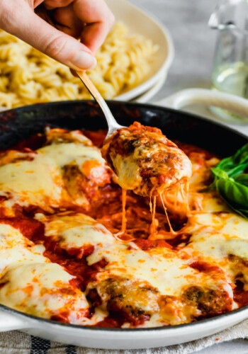 A spoon scooping skillet chicken parmesan with melty cheese.