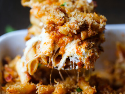 A spoonful of cheesy baked mostaccioli is served from a casserole dish.