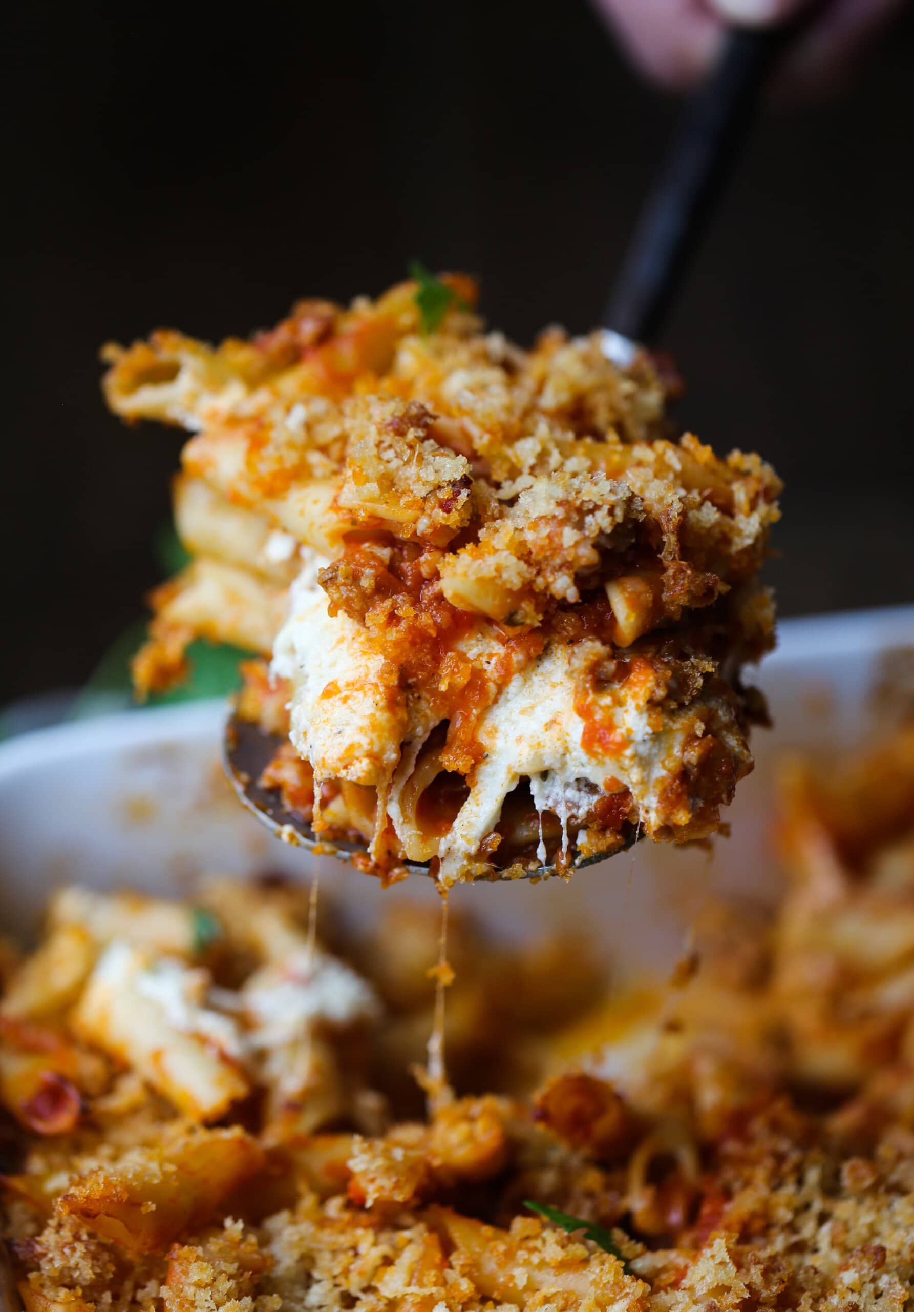 A spoonful of cheesy baked mostaccioli is served from a casserole dish.