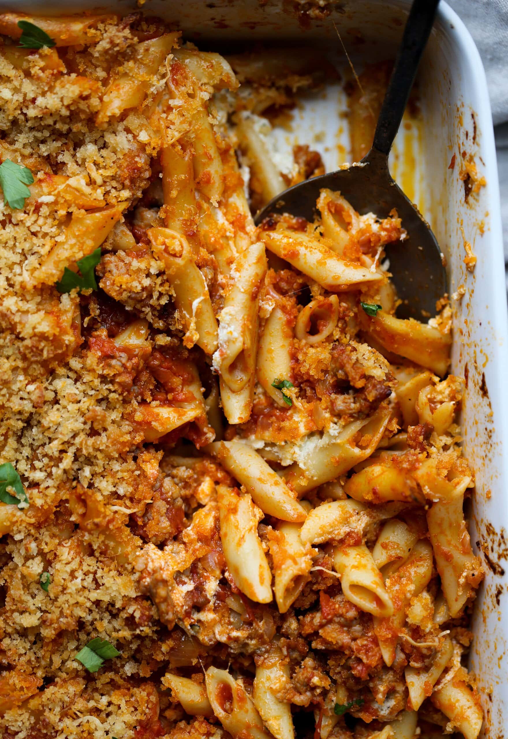 Baked mostaccioli pasta is scooped from a casserole dish.
