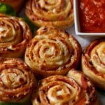 Homemade pizza rolls next to a bowl of pizza sauce for dipping.