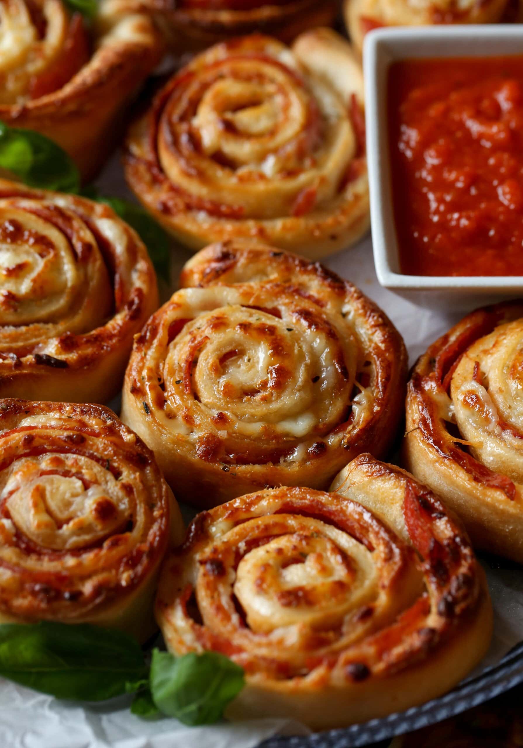 Homemade pizza rolls next to a bowl of pizza sauce for dipping.