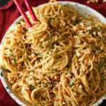 A bowl of spicy sesame noodles with chopsticks.