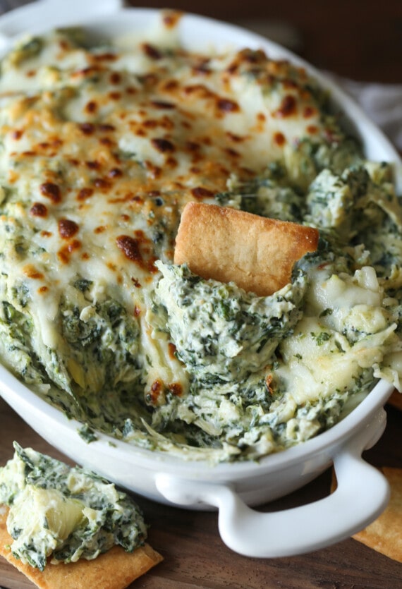 A pita chip is used to scoop creamy spinach and artichoke dip.