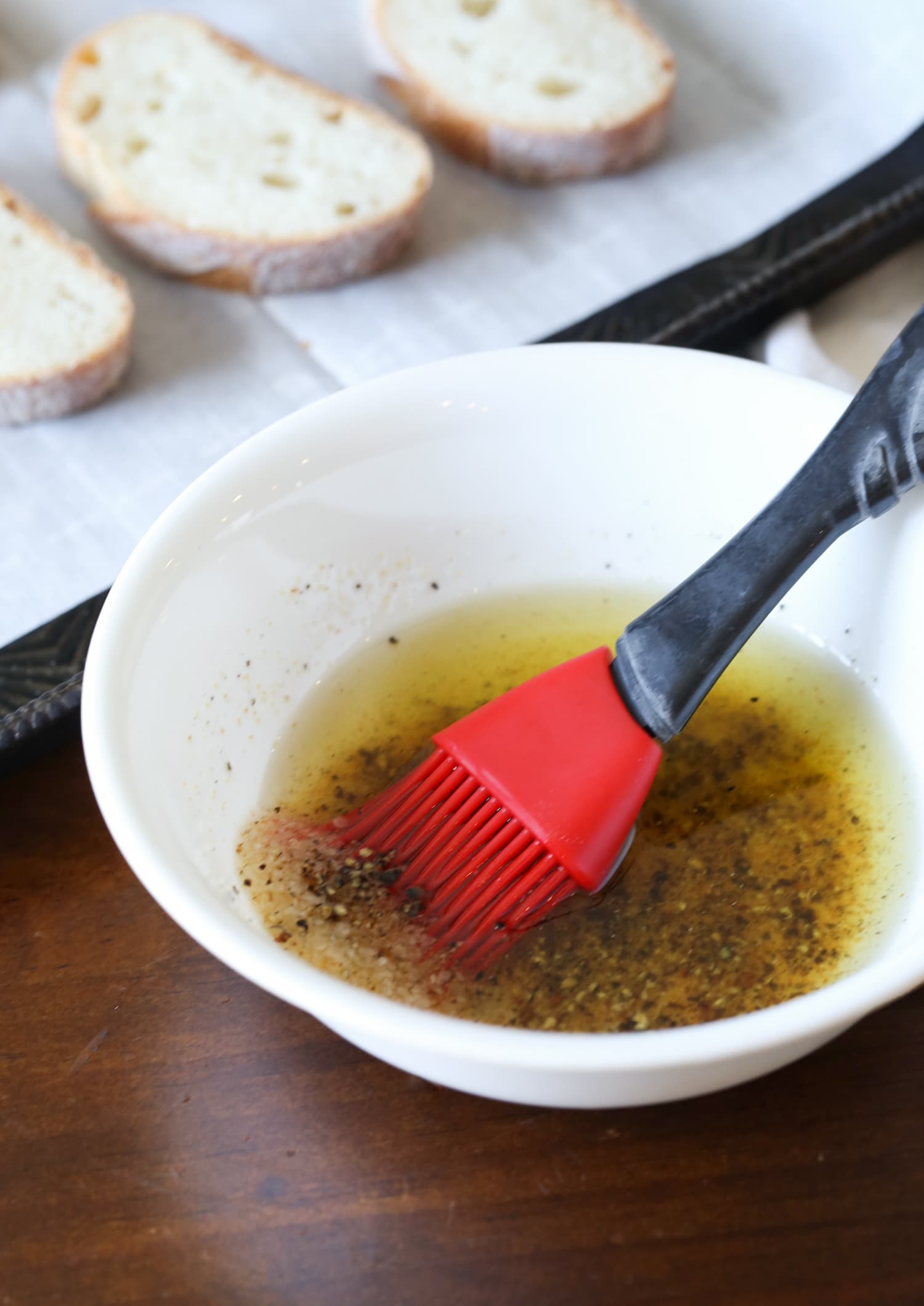 A mixture of olive oil and seasonings in a bowl with a pastry brush.