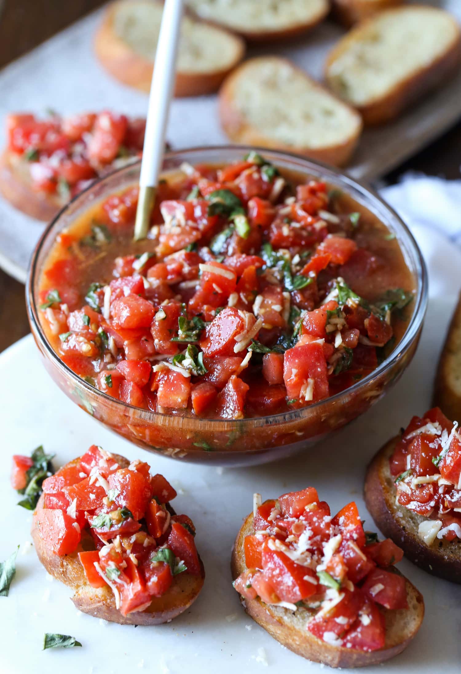 A bowl of bruschetta surrounded by bruschetta toasts.