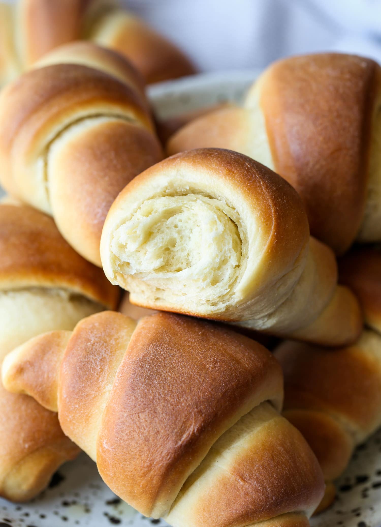 A pile of homemade crescent rolls, one with a bite missing.