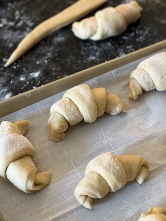 Rolled crescent dough on a parchment-lined baking sheet.