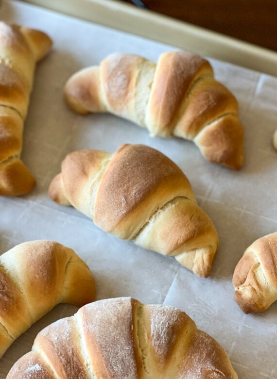 Homemade crescent rolls on a parchment-lined baking sheet.