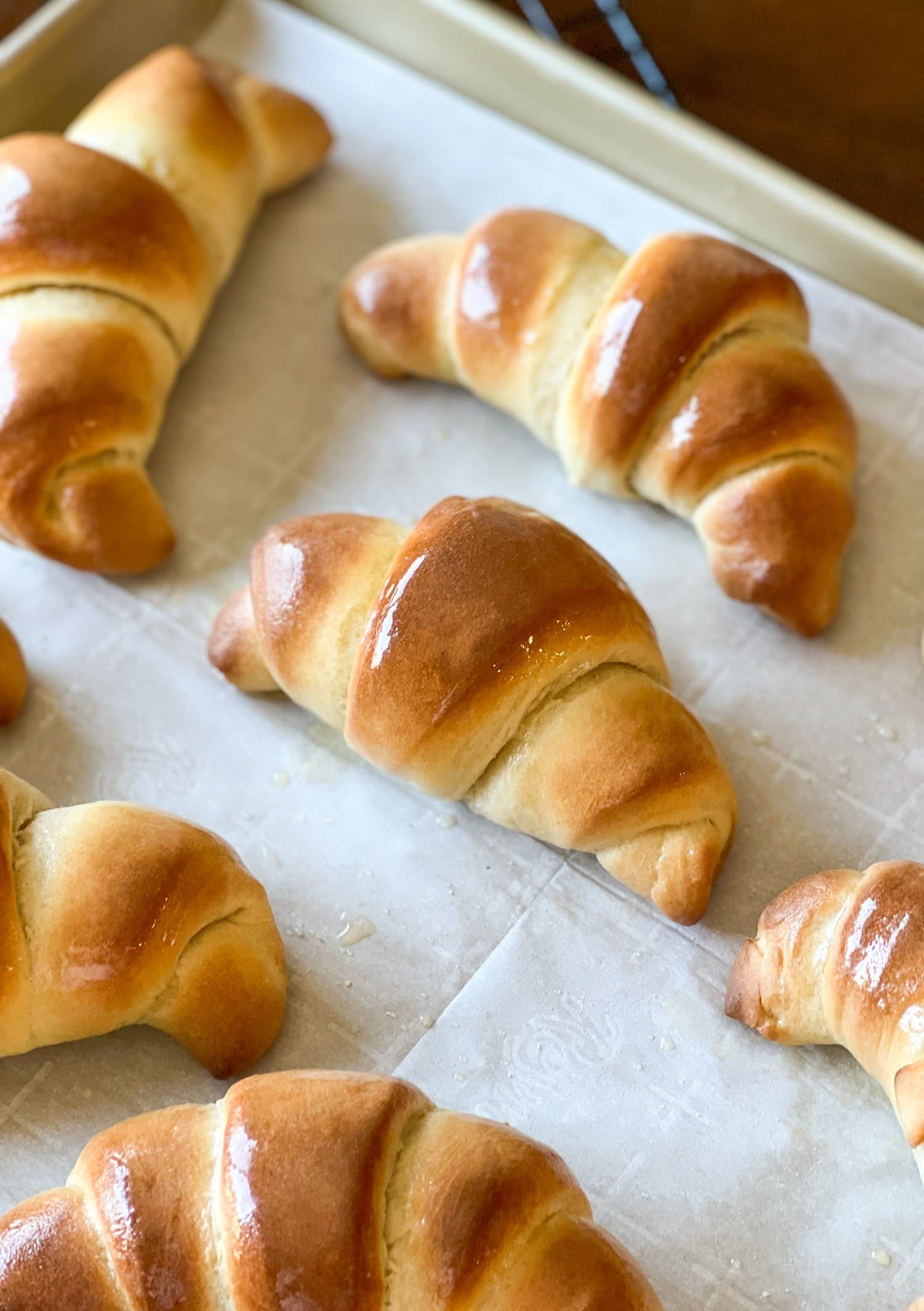Homemade crescent rolls glazed with butter on a parchment-lined baking sheet.