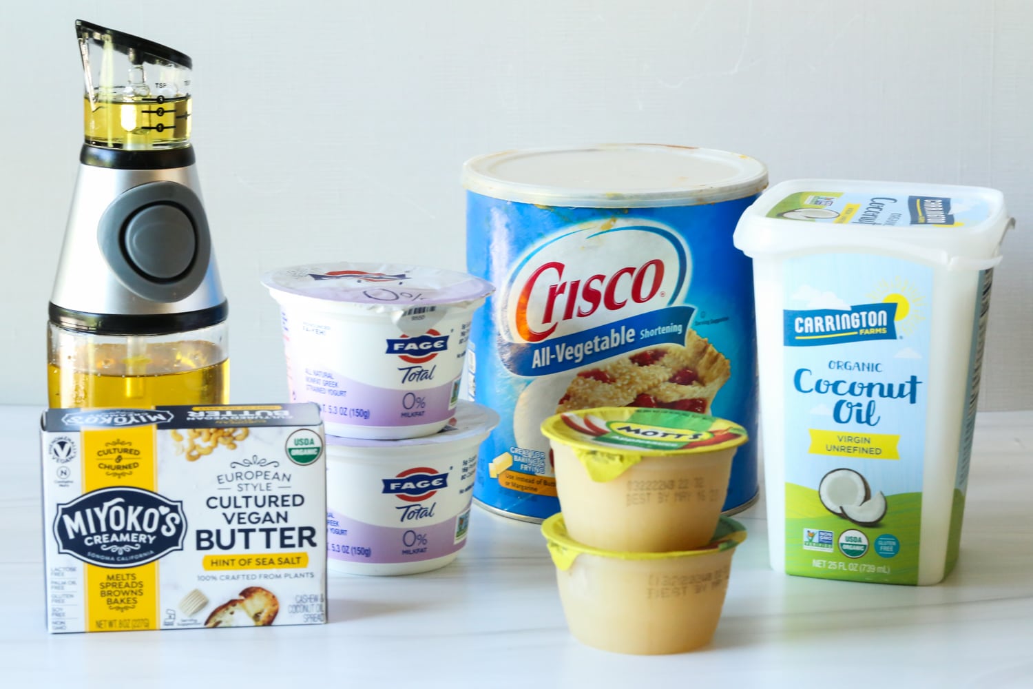olive oil, vegan butter, applesauce, shortening, greek yogurt, and coconut oil on a counter