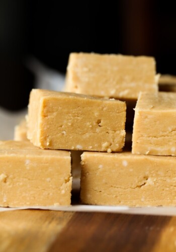 Peanut butter fudge squares stacked on top of each other on a piece of parchment paper.