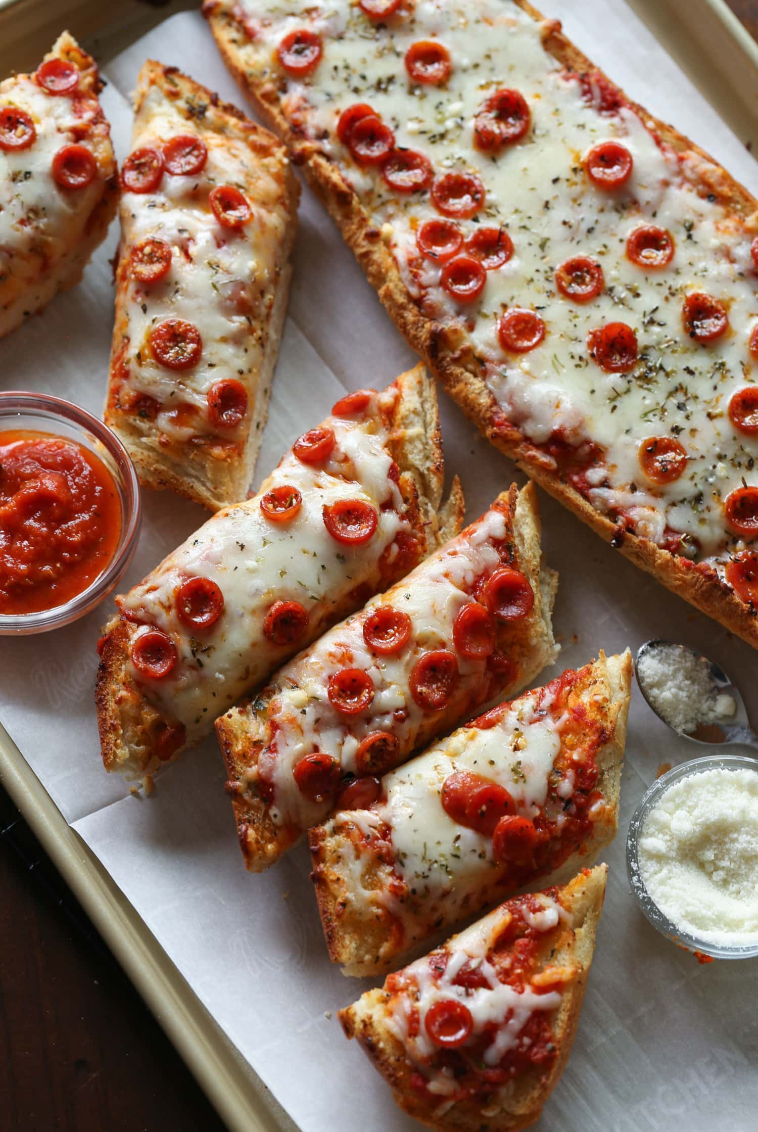 French bread pizza cut into individual slices on a platter, next to dipping sauces.