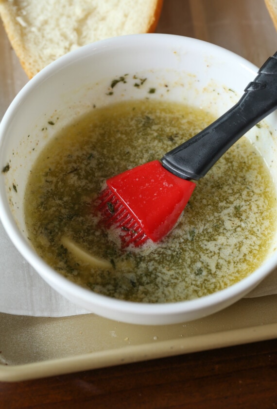 Melted garlic butter in a white bowl with a silicone brush.