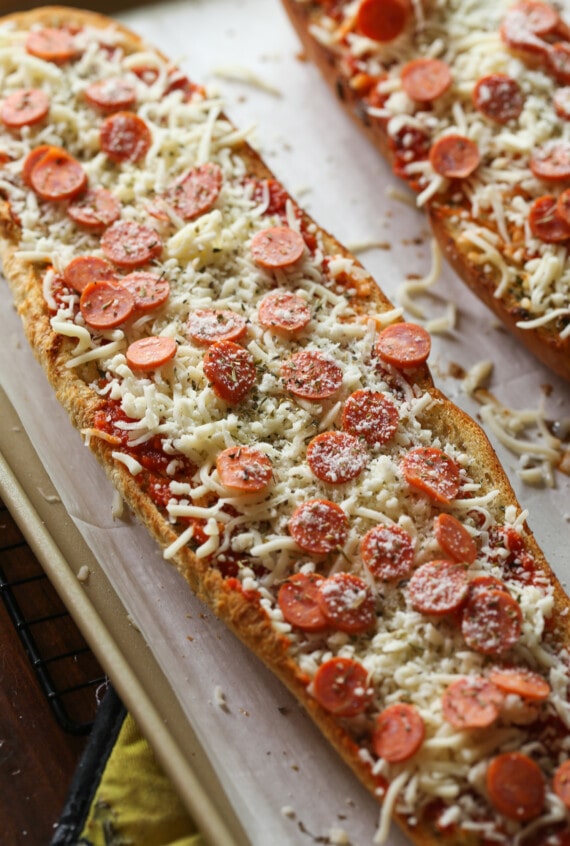 Two French bread pizzas topped with cheese and pepperoni slices on a baking sheet.