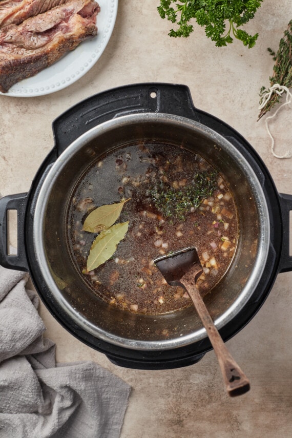Brühe, Kräuter, Zwiebeln und Knoblauch kombiniert in einem Instant Pot.