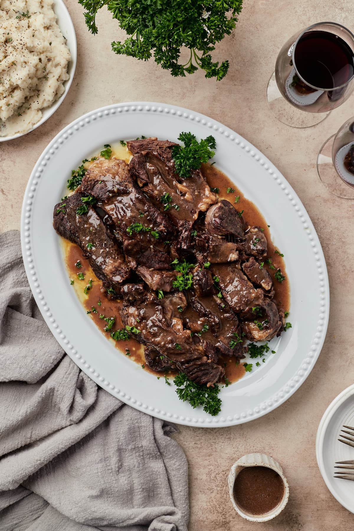 A table spread featuring juicy beef short ribs covered in red wine sauce on a white dish.