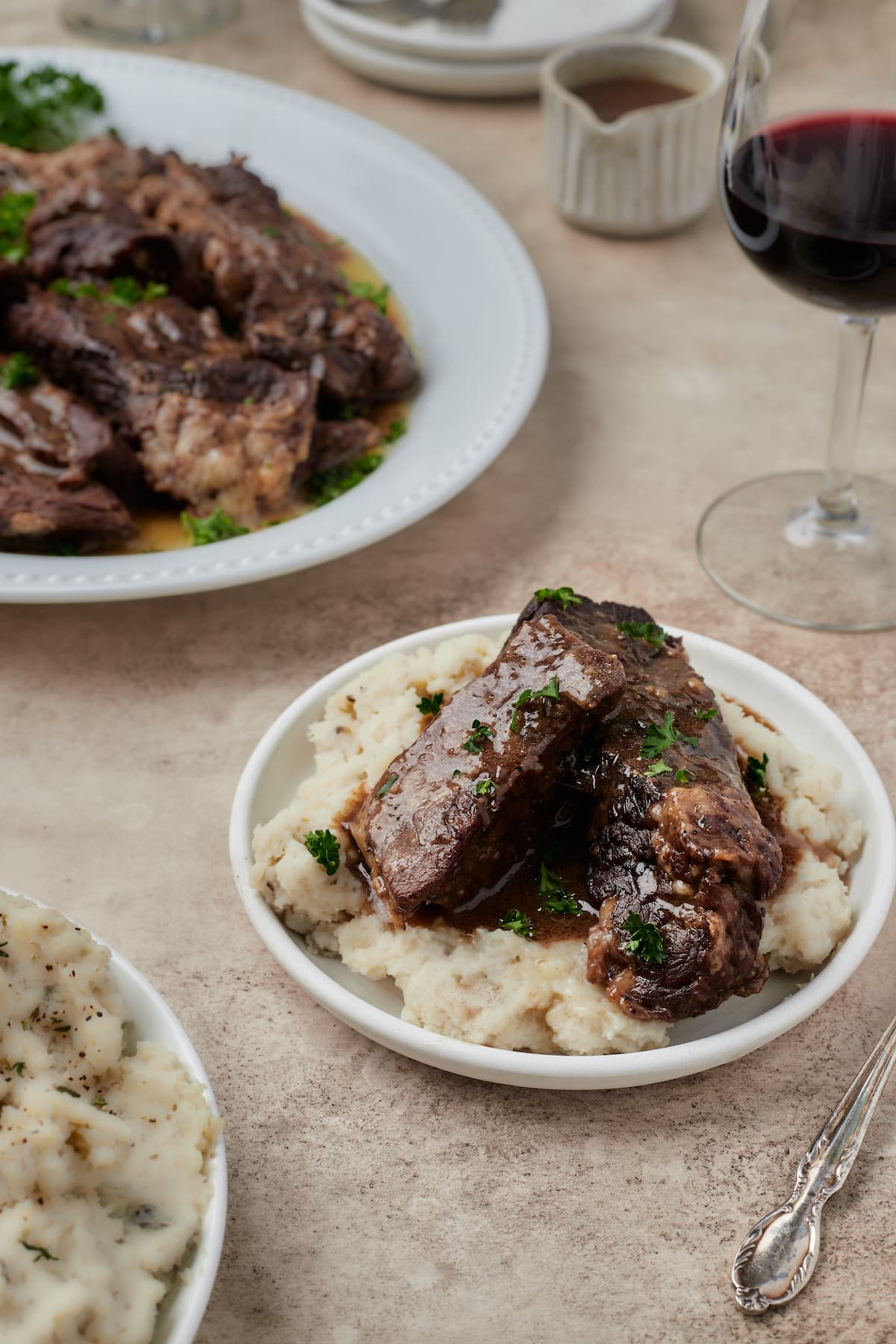 Instant Pot short ribs served in a bowl over mashed potatoes, with a platter of short ribs in the background.