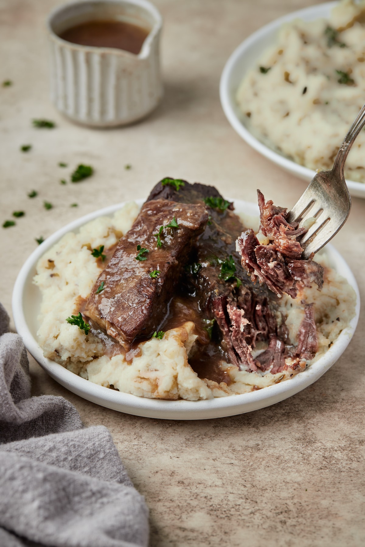 A fork picking up an Instant Pot short rib served in a bowl over mashed potatoes.