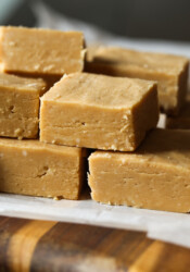 Peanut butter fudge squares stacked on top of each other on a piece of parchment paper.