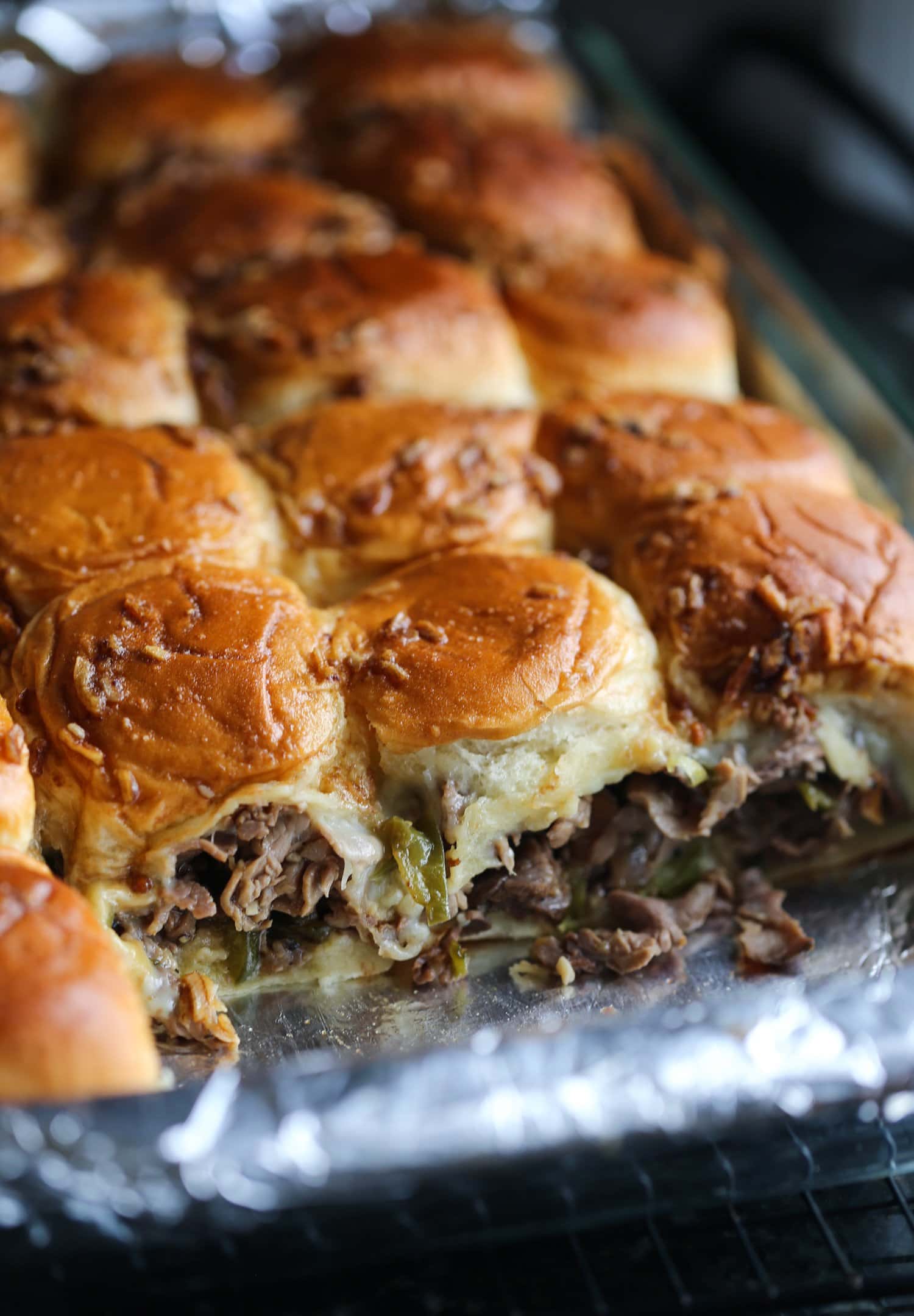 Philly cheesesteak sliders in a baking dish with one row missing.