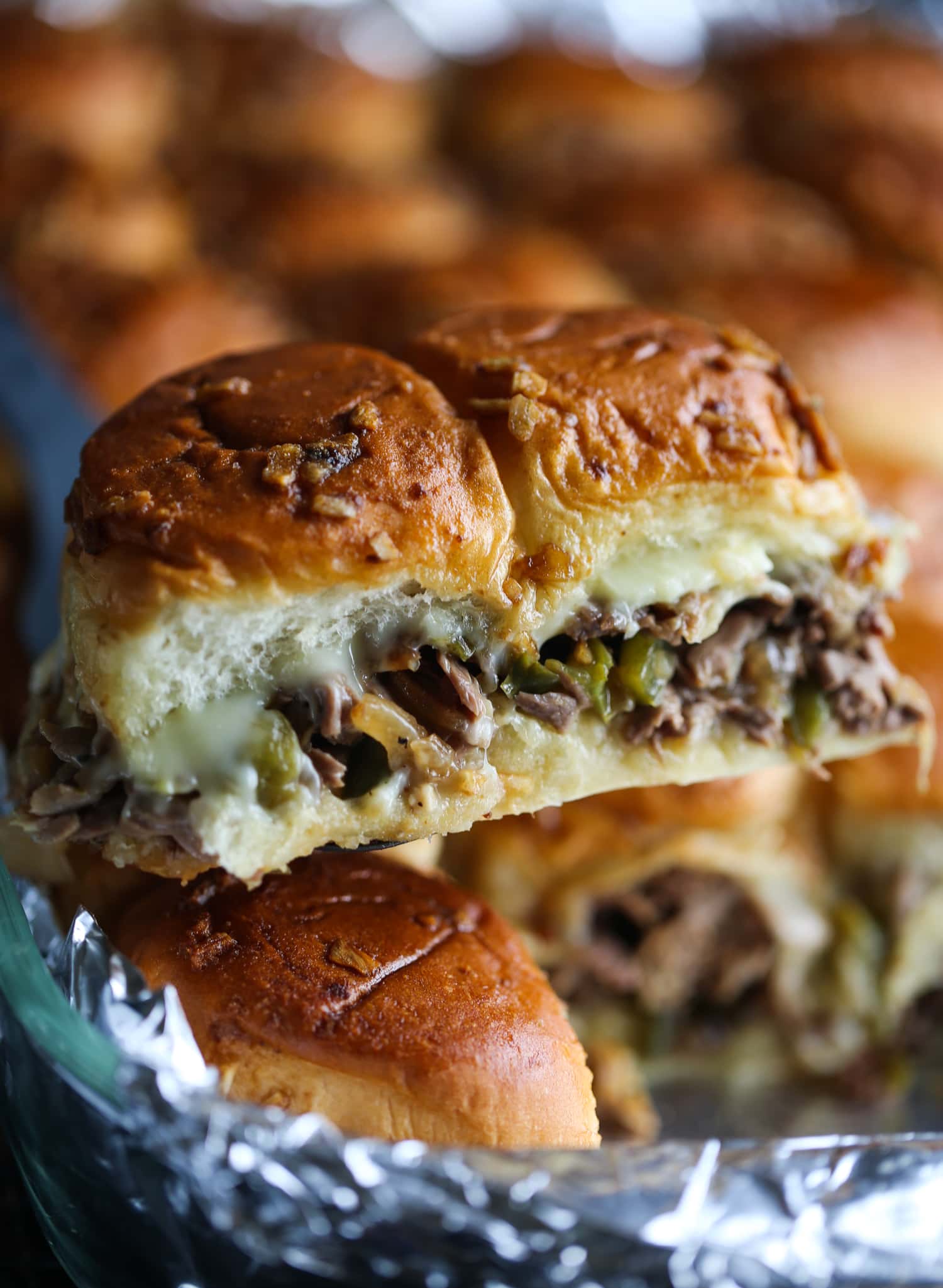 Two cheesesteak sliders are scooped from the pan.
