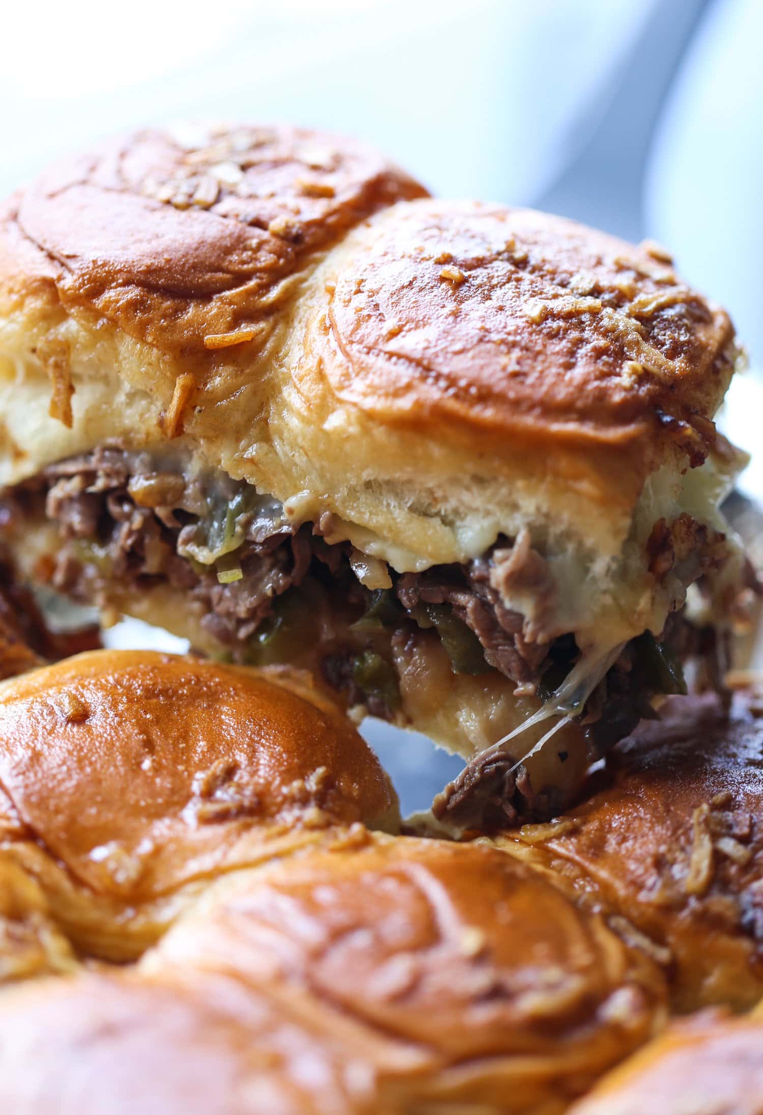 Two Philly cheesesteak sliders are scooped from the pan.